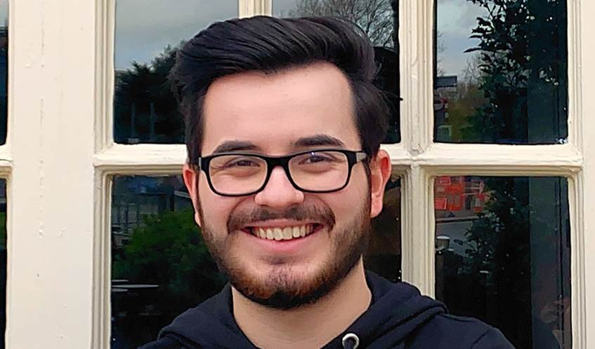 A man with dark hair and a beard, wearing glasses, smiles at the camera.