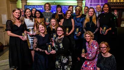 A large group of women gathered holding awards smiling at the camera.