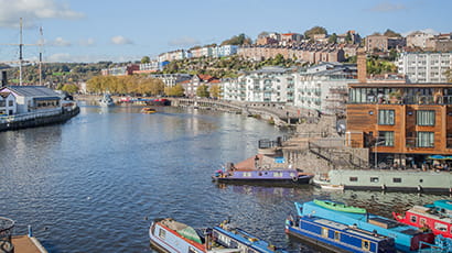 Image of Bristol waterfront with boats and buldings against the backdrop of a blue sky.