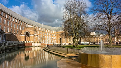 Image of Bristol City Hall with a fountain and water feature in the foreground on a sunny day.