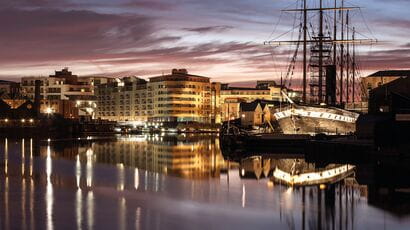 Brunel's SS Great Britain in Bristol Harbour at dusk with lights reflecting on the water.