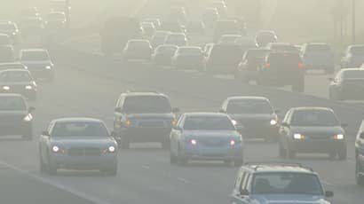 Image of a busy multi-lane road with lots of cars in busy traffic surrounded by smog or polluted air.