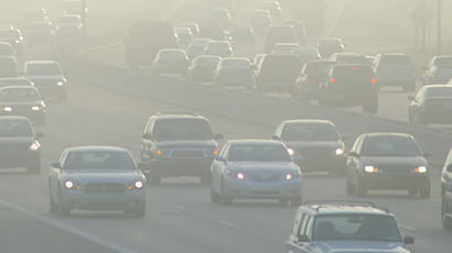 Image of a busy multi-lane road with lots of cars in busy traffic surrounded by smog or polluted air.