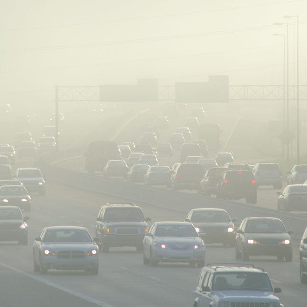 Image of a busy multi-lane road with lots of cars in busy traffic surrounded by smog or polluted air.