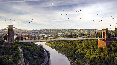 Aerial shot of the Clifton Suspension Bridge and the gorge with many hot air balloons in flight.