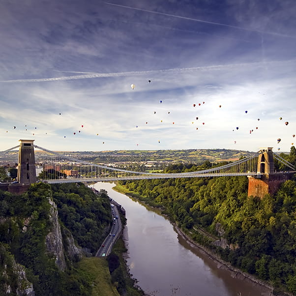 Aerial shot of the Clifton Suspension Bridge and the gorge with many hot air balloons in flight.