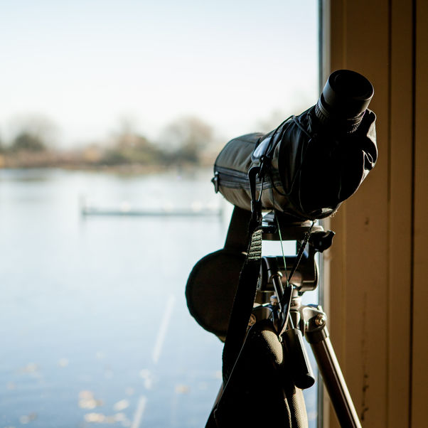 A camera set up on a tripod facing outwards through a window at a large pond.