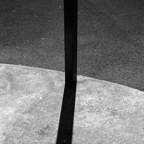 Black and white photo of a pole, with a shadow.
