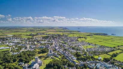 Drone aerial photo landscape of a town with green fields, coast and sea against a blue sky.