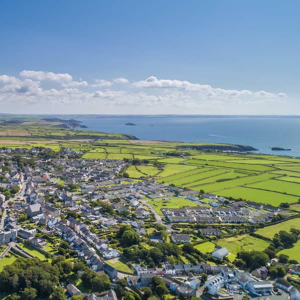 Drone aerial photo landscape of a town with green fields, coast and sea against a blue sky.