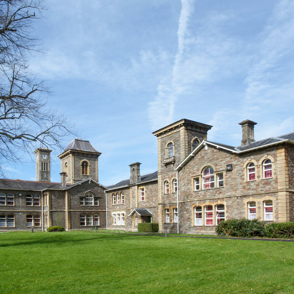 Exterior photograph of a large stone building seen through the gardens and magnolia tree at UWE Bristol Glenside Campus.