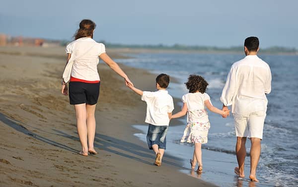 Young family of a mother, father and two small children walking on the beach.