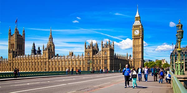 People walking  with Big Ben and Houses of Parliament in the background against a blue sky.