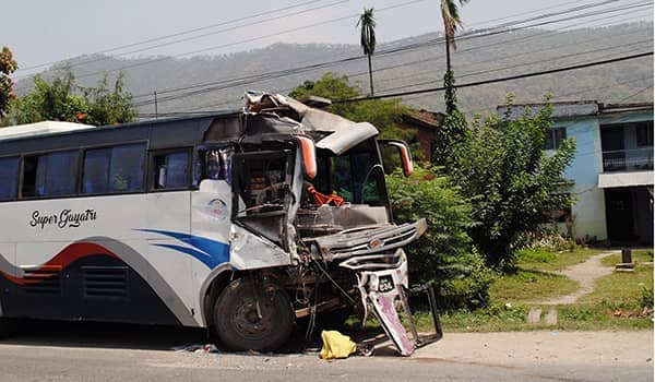 Side shot of a bus post-accident parked by the side of a residential road with the front of the bus smashed in.