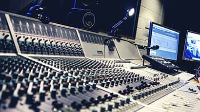The interior of a sound recording studio with a large panel of control buttons  with multiple computer screens.
