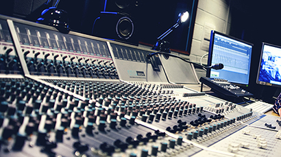 The interior of a sound recording studio with a large panel of control buttons  with multiple computer screens.