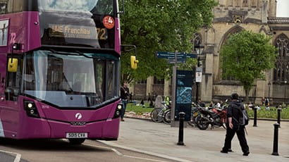 View of Bristol Cathedral with pedestrians and a First bus on the UWE Frenchay route in the foreground. There are trees and a bike park.