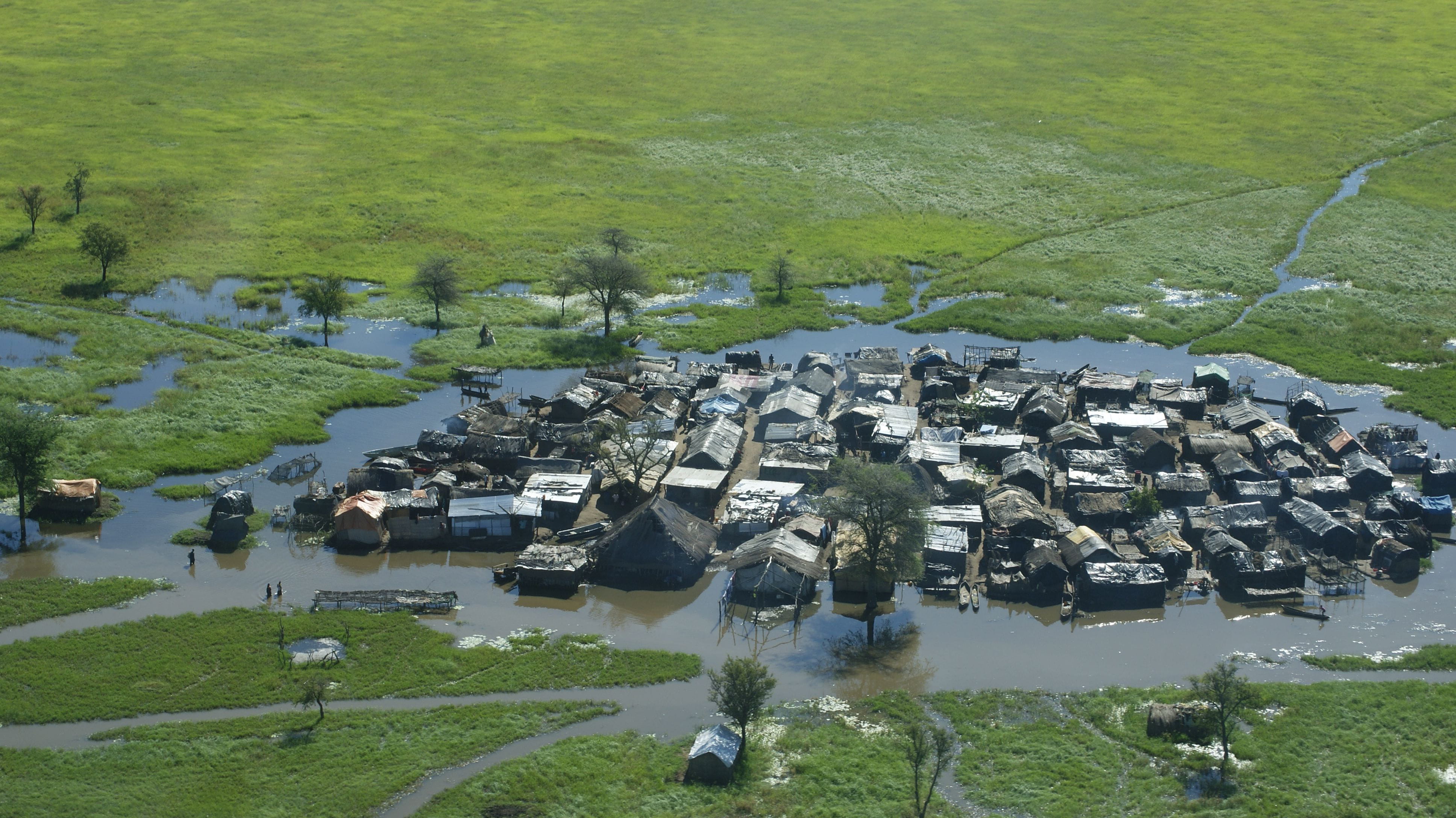 Aerial shot of a flooded village surrounded by a green field.