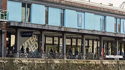 Image of The Watershed at the Bristol Harbourside in the daylight with a metal chain in the foreground and people walking past in the background.