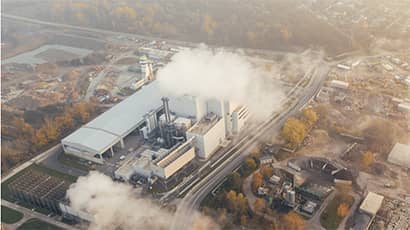 Image of a industrial building producing plumes of smoke and pollution in the midst of a city landscape.