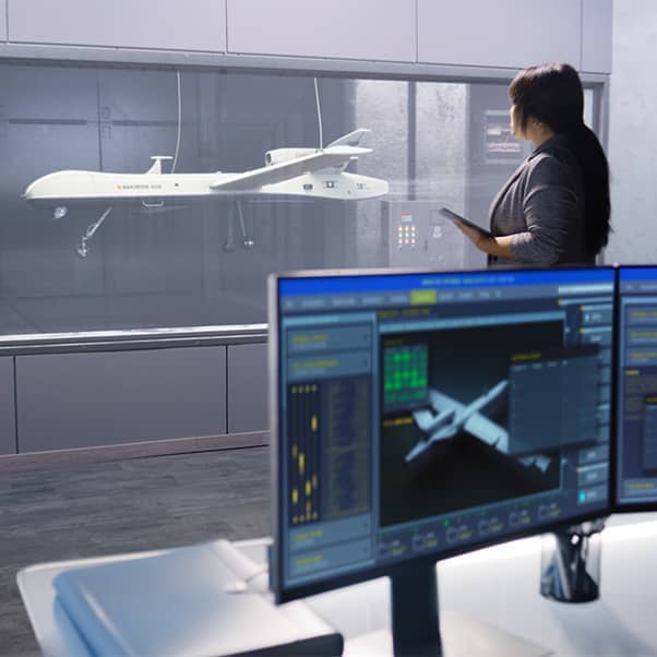 A female engineer checks aerodynamics of a drone in a laboratory using a wind tunnel with a computer monitor in the foreground.