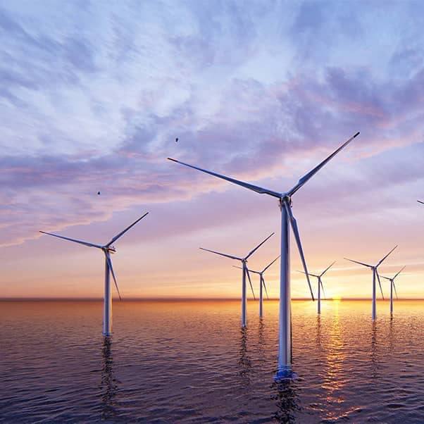 Offshore wind turbines farm on the ocean against a sunset sky.