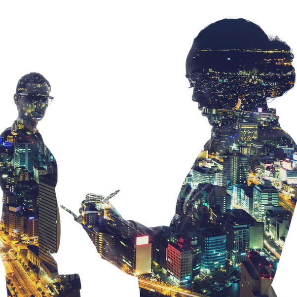 Silhouettes of business people against a backdrop of a night time city skyline.
