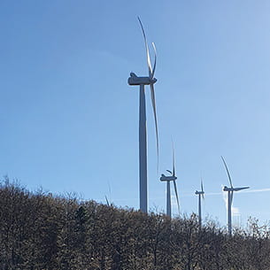 A row of wind turbines on a grassy slope with blue skies in the background.
