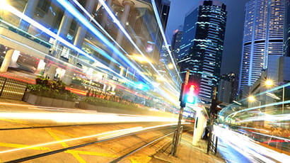 Dutch angled shot of an urban city scene at night with illuminated light trail against a backdrop of tall buildings.