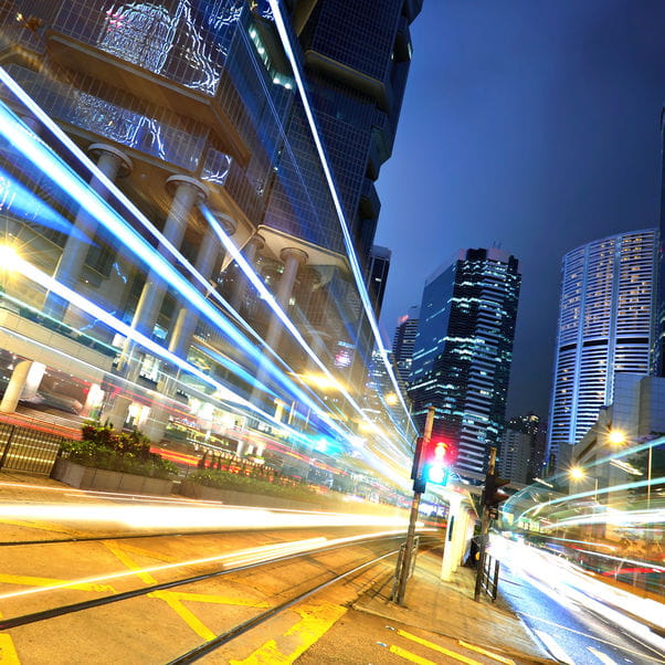 Dutch angled shot of an urban city scene at night with illuminated light trail against a backdrop of tall buildings.