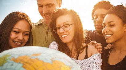 Photo of a group of people of mixed race and gender looking and holding a globe.