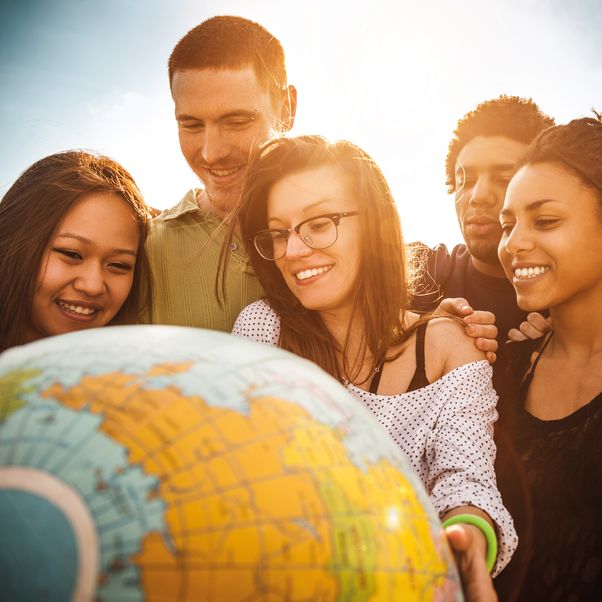 Photo of a group of people of mixed race and gender looking and holding a globe.