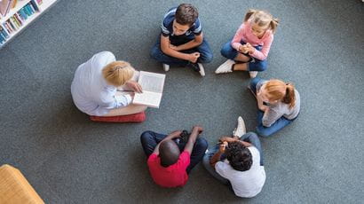 Children sat in a circle while an adult reads to them.