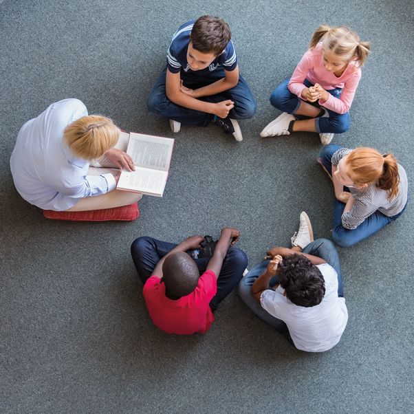 Children sat in a circle while an adult reads to them.