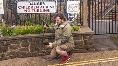 Image of UWE Bristol PhD student, Louis Brown, kneeling on a street pavement collecting data of pollutant concentrations.