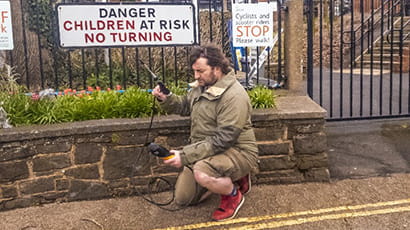 Image of UWE Bristol PhD student, Louis Brown, kneeling on a street pavement collecting data of pollutant concentrations.