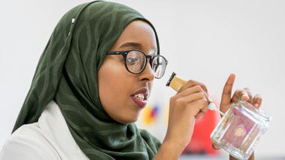 Student inspecting a glass bottle while wearing a white coat.