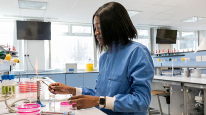Student working in a lab while wearing a blue coat.