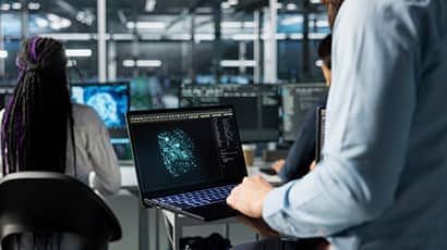 Close up shot of of a male in a server hub optimizing performance through AI assistant analysis with a seated female.