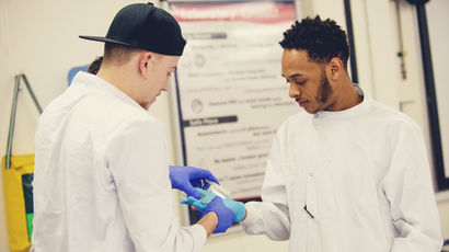 Two students wearing white lab coats handling gloves.