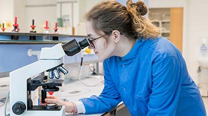 Biology student sat in a lab looking through a microscope.