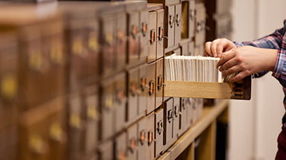 image of card filing drawers with one open, and a pair of hands seeking a card.