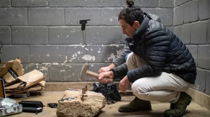 Project at the creative economies lab, person crouching next to a large stone hammering pegs into it.
