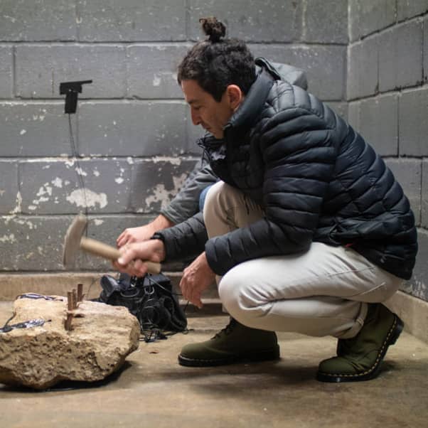 Project at the creative economies lab, person crouching next to a large stone hammering pegs into it.