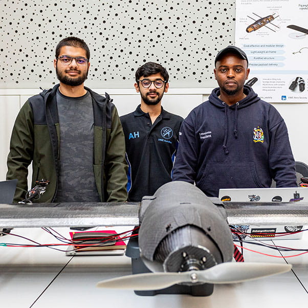 Three male students standing proudly behind a propeller aircraft prototype at the UWE Degree Show.