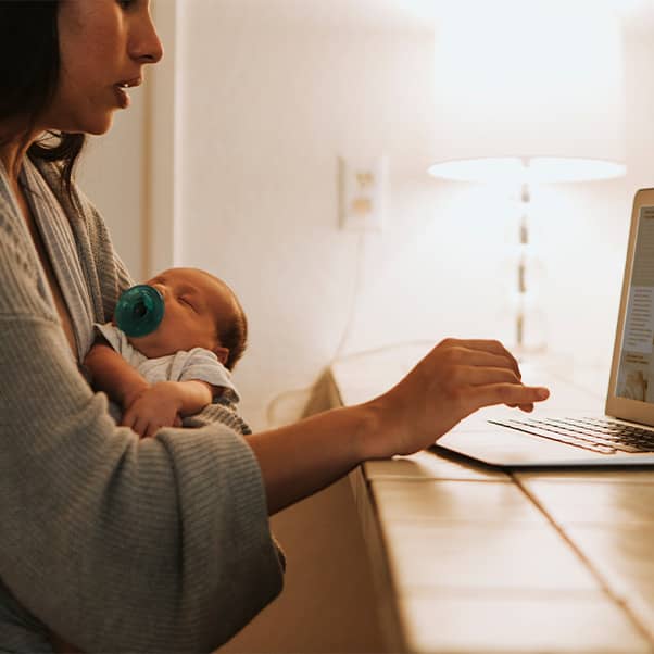 Mother holding new born while working on a laptop.