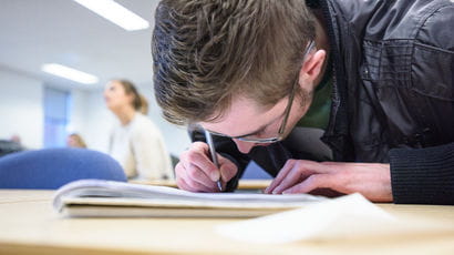 Close up image of a student writing with their head down