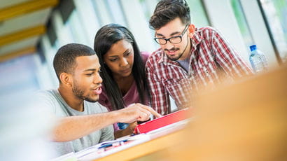 Three students huddled together discussing work