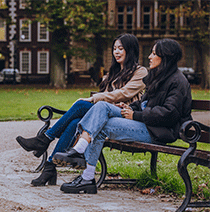 Two students sat on a bench together talking in Bristol's Queens Square.