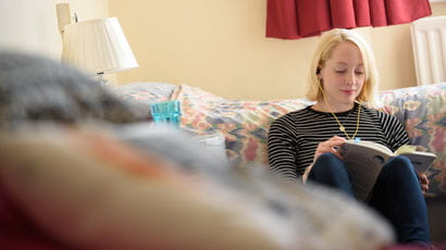Student with headphones in reading in university accommodation room